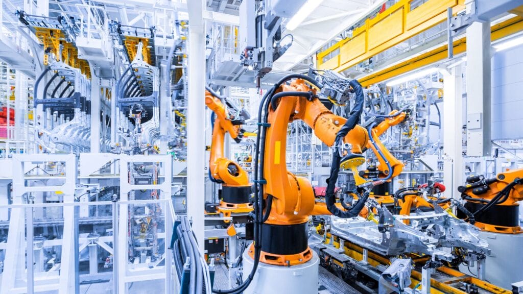 A modern manufacturing facility featuring bright orange robotic arms operating on an assembly line, surrounded by intricate industrial machinery, symbolizing innovation and efficiency in global manufacturing processes