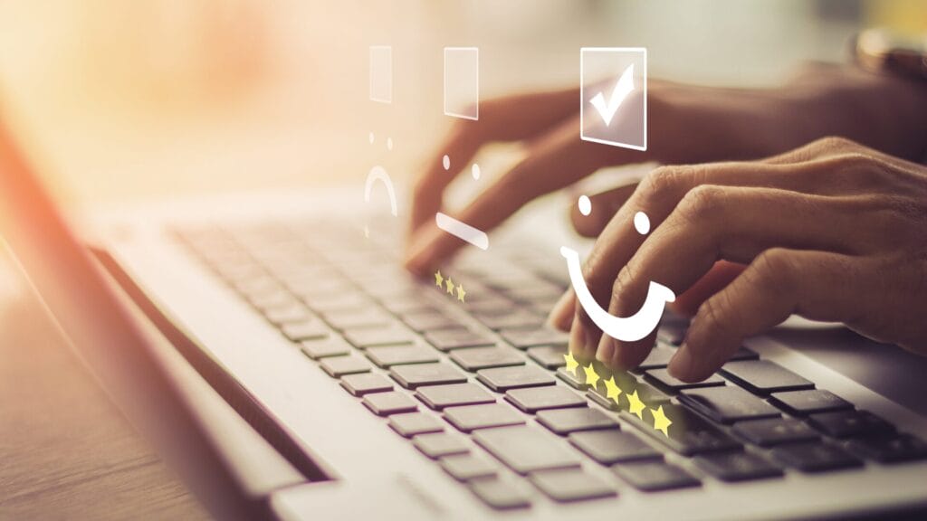 "Hands typing on a laptop keyboard with overlaid smiley face icons representing customer satisfaction, including stars and a checkmark, symbolizing positive feedback and live chat support."